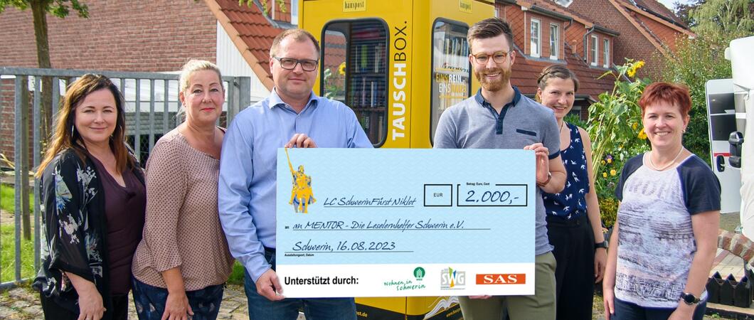 Vor der Büchertauschbox überreichten Babette Herrmann, Susanne Jenczewski und Jens Leupold vom Lions Club Fürst Niklot (v.l.) den Spendencheck an Claudia Milius, Neele Jepsen und Alexander Kieslich vom MENTOR e.V. (v.r.), Foto: maxpress