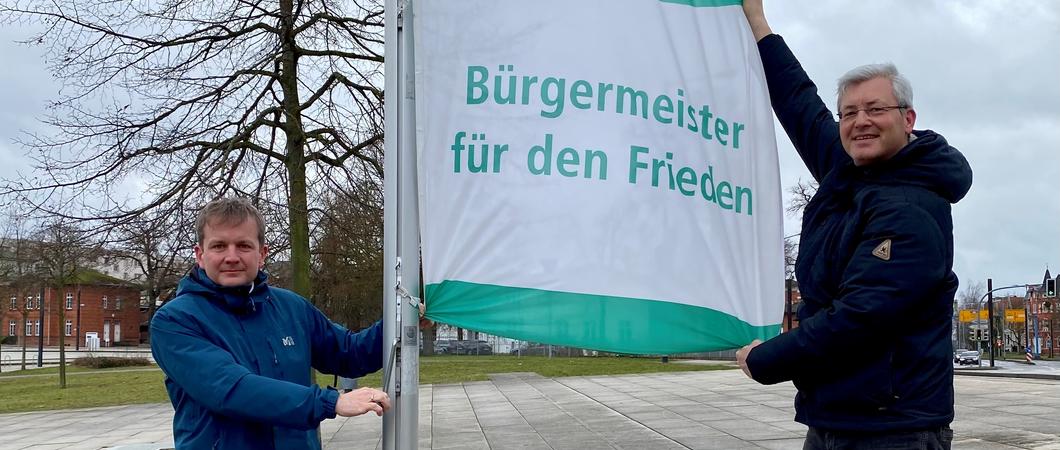 Schwerins Oberbürgermeister Rico Badenschier und der stellvertretende Stadtpräsident Daniel Meslien am Freitag auf dem Bertha-Klingberg-Platz die Flagge der Organisation „Mayors for Peace - Bürgermeister für den Frieden