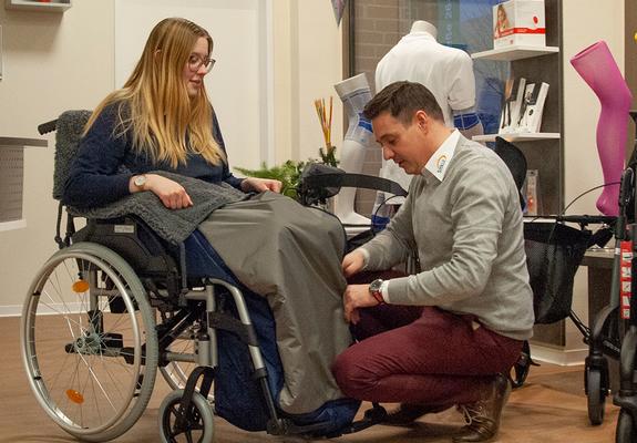 Medizinproduktberater Jens Goldenbohm zeigt einer Kundin den Schlupfsack für Rollstühle